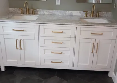 A white bathroom with marble counter tops and gold faucets.