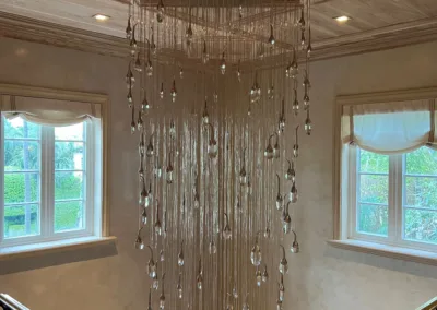 A chandelier hangs from a staircase in a home.